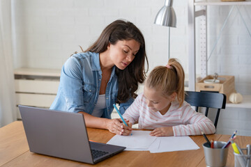 Mother and daughter learning together at home, sitting at the desk in front of a computer. Back to school