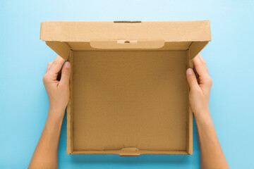 Woman hands holding opened brown carton box on blue table background. Closeup. Empty place for...