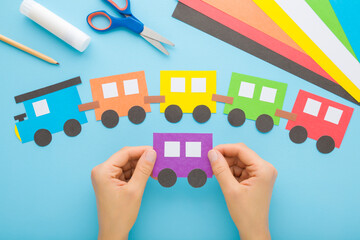Young adult woman hands holding and showing colorful paper train with wagons on light blue table...