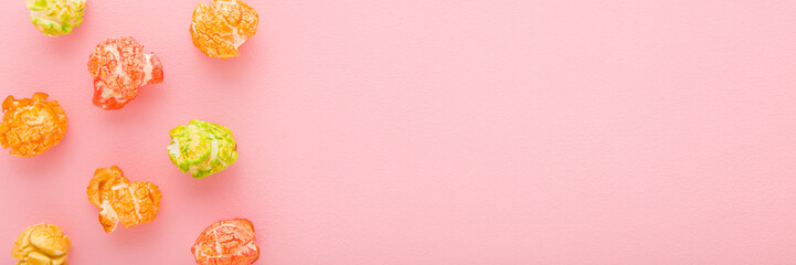 Colorful sweet popcorn on light pink table background. Pastel color. Wide banner. Closeup. Sweet...