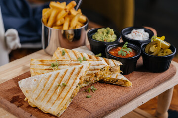 Chicken Quesadillas taco wrap slice with chili sauce and french fries bucket served on wooden board...