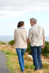Old couple, walking and holding hands in nature on holiday, vacation or retirement with support. Back, man and woman with love, care and happiness in marriage together on a road, journey or path