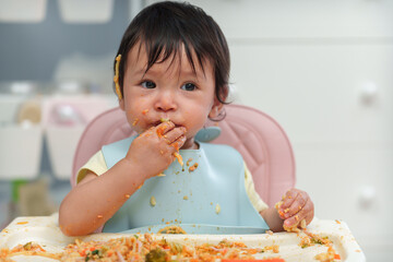 infant baby eating food and vegetable by self feeding BLW or baby led weaning on chair