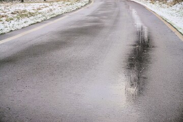 Spiegelglatte Straße mit Spiegelung von Baum zwischen Schneebedeckten Feldern bei Kälte, Eis und...