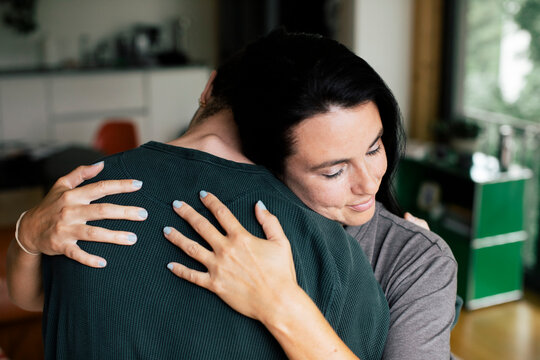 Mother with eyes closed embracing son at home