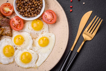 Delicious nutritious breakfast of fried quail eggs, bacon, legumes and cherry tomatoes