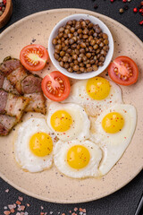 Delicious nutritious breakfast of fried quail eggs, bacon, legumes and cherry tomatoes