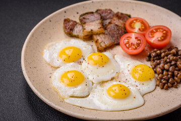 Delicious nutritious breakfast of fried quail eggs, bacon, legumes and cherry tomatoes
