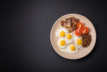 Delicious nutritious breakfast of fried quail eggs, bacon, legumes and cherry tomatoes