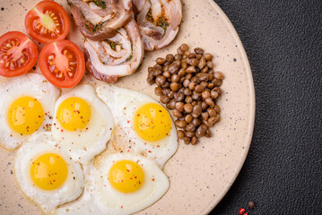 Delicious nutritious breakfast of fried quail eggs, bacon, legumes and cherry tomatoes