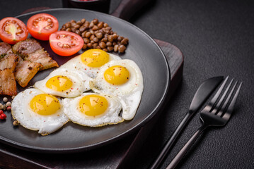 Delicious nutritious breakfast of fried quail eggs, bacon, legumes and cherry tomatoes