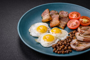 Delicious nutritious breakfast of fried quail eggs, bacon, legumes and cherry tomatoes