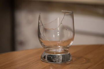 Broken transparent drinking glass on the table. Sharp dangerous pieces in the kitchen.