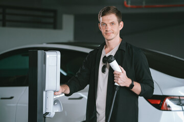 Young man travel with EV electric car to shopping center parking lot charging in downtown city...