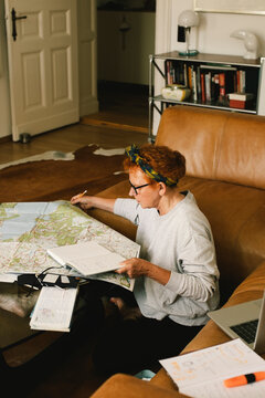 Side view of elderly woman planning trip on map while sitting in living room at home
