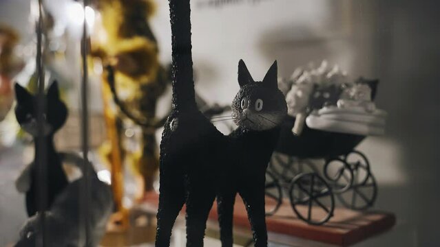 A cool black toy cat stands in the window with its tail up. A cool toy in the form of a cat