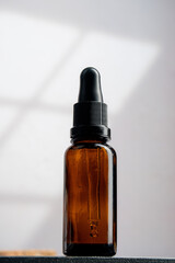 Cosmetic bottles made of dark amber glass on white background with window leaves shadow.