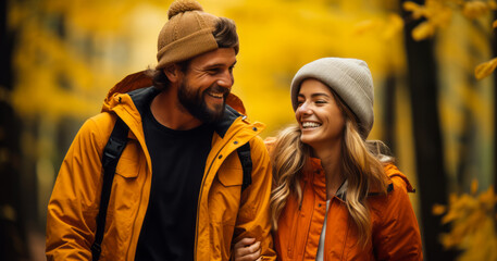 Joyful couple in warm autumn outfits holding hands while walking through a forest with golden yellow foliage, embodying happiness and active lifestyle