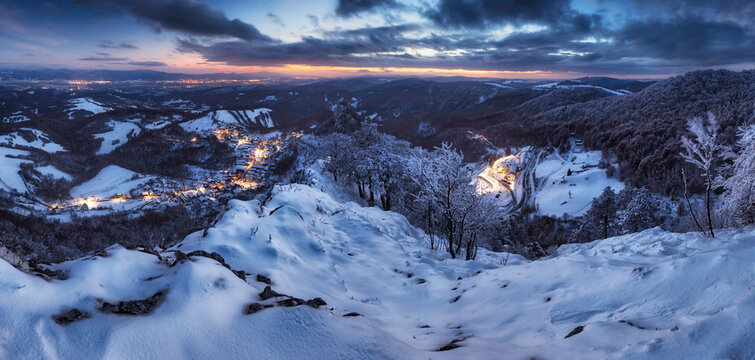 Panorama of night Carpathian winter mountain village in light with wooden houses on a hill covered with fresh snow.