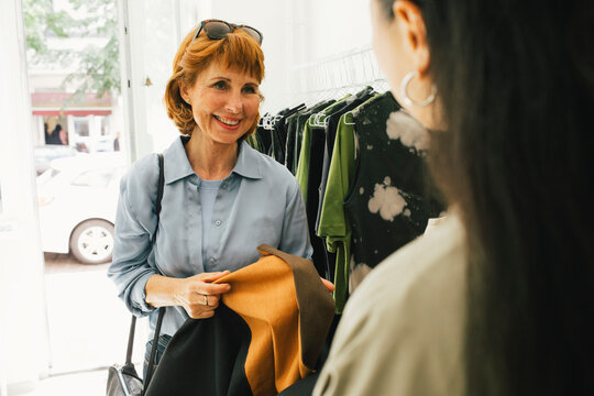 Smiling senior customer talking with female sales staff while shopping at clothes store