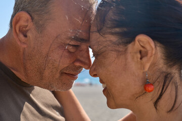 Closeup portrait of happy middle aged couple enjoying romantic moment on the beach. Mature man and woman looking into each other's eyes, touching their foreheads together before kiss near seaside.
