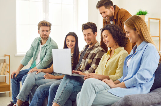 Portrait Of Cheerful Happy Friends Students Sitting On Sofa Watching Funny Movie On A Laptop Or Having Video Call At Home And Laughing. Young Guys And Girls Enjoying Spending Time Together.