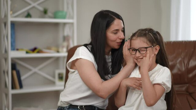 Mom shares secrets with her daughter, telling her in her ear. Joyful communication between mother and daughter