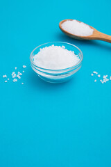 Wooden spoon with salt and glass bowl on the bright blue background