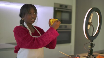 in home kitchen a young african american woman engages with social media, talking on healthy eating and vegetarian cooking while looking at her mobile phone