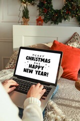 Young woman working on a laptop, Merry Christmas and New Year greetings on the screen