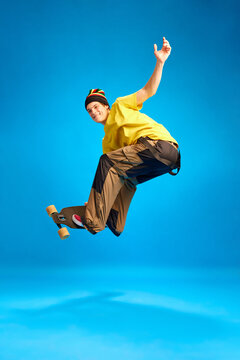 Positive, smiling man wearing in rastaman, reggie style doing Ollie trick in motion against blue background.
