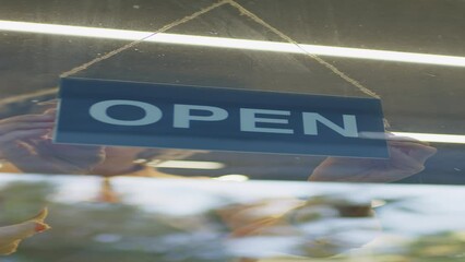 Vertical through glass door shot of Caucasian female supermarket worker approaching to door and turning around hanging sign, opening store for customers in morning