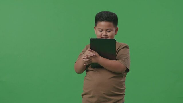 An Asian Boy Smiling While Using Tablet On Green Screen Background In The Studio
