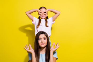 Photo of irritated funky little sisters wear t-shirts fooling trying relax empty space isolated yellow color background