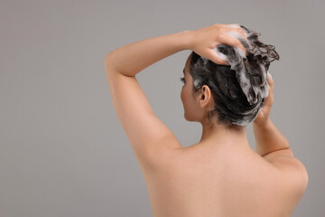 Fototapeta premium Woman washing hair on grey background, back view. Space for text