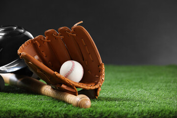 Baseball bat, batting helmet, leather glove and ball on green grass against dark background. Space for text - obrazy, fototapety, plakaty