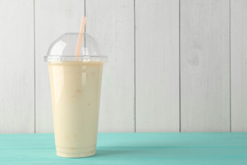 Tasty smoothie in plastic cup on light blue table against white wooden wall. Space for text