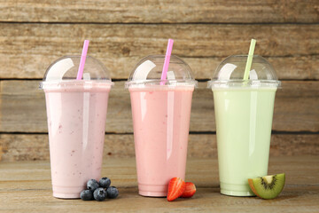 Plastic cups with different tasty smoothies and fresh fruits on wooden table