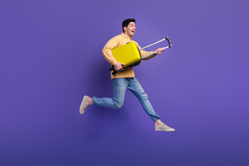 Fototapeta na wymiar Full length photo of handsome young guy running hold baggage adventure wear trendy yellow garment isolated on violet color background