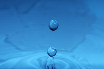 Drop falling into water on blue background, macro view