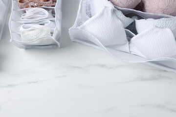 Organizers with folded women's underwear on white marble table, flat lay. Space for text