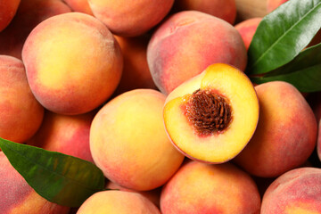 Cut and whole fresh ripe peaches with green leaves as background, top view