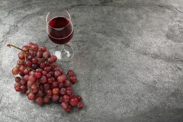 Delicious fresh red grapes and glass of wine on grey textured table. Space for text