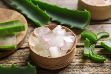 Aloe vera gel and slices of plant on wooden table, closeup