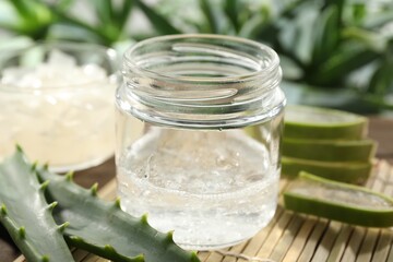 Aloe vera gel in jar and slices of plant on bamboo mat, closeup