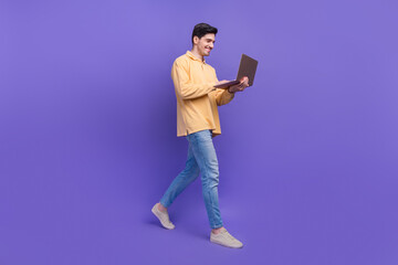 Full body photo of nice young male walk hold netbook eshopping wear trendy yellow outfit isolated on violet color background