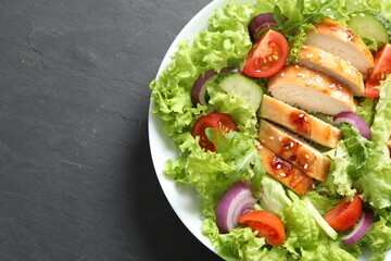 Delicious salad with chicken and vegetables on black table, top view. Space for text