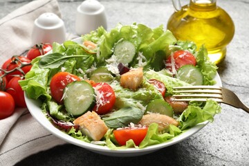 Eating delicious salad with chicken, cheese and vegetables at grey table, closeup