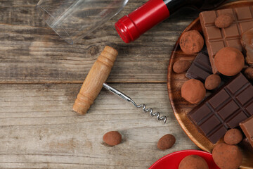 Bottle of red wine, glass, chocolate sweets and corkscrew on wooden table, flat lay. Space for text