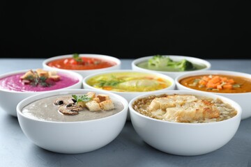 Different cream soups and tasty broth in bowls on gray table, closeup